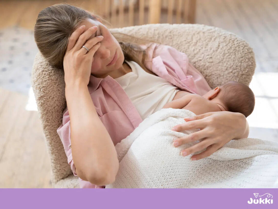 Zmęczona mama trzymająca się za głowę podczas karmienia piersią, sugerująca potrzebę pielęgnacji i przygotowania brodawek.
