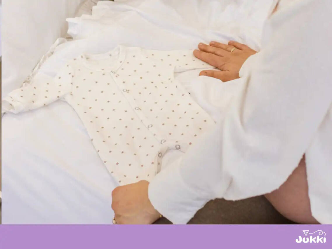 Białe body niemowlęce w gwiazdki rozłożone na łóżku przez mamę.